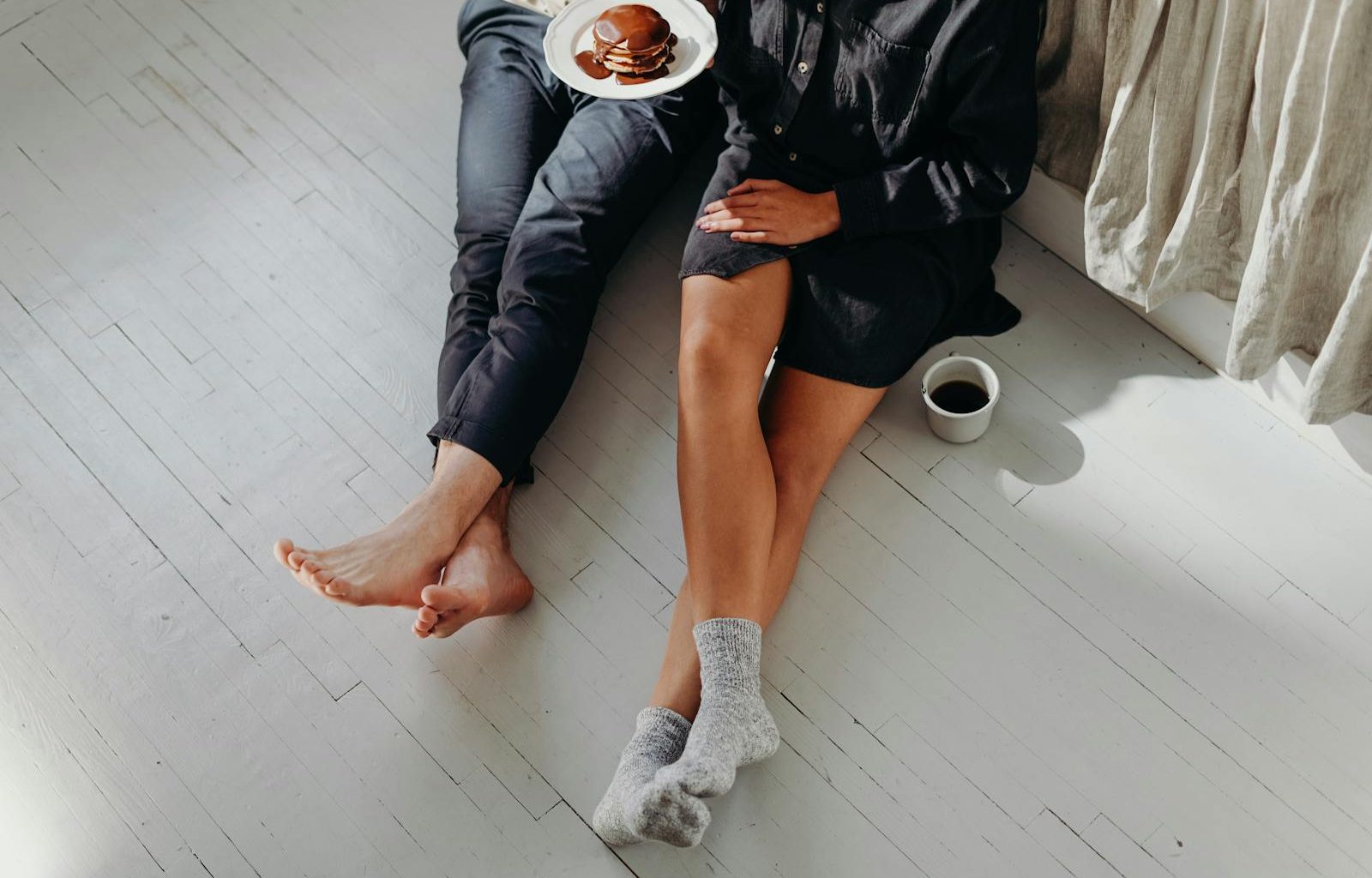A cozy couple enjoying a quiet breakfast with pancakes and coffee on a sunlit floor.