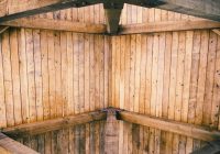 Warm woonboerderij interieur met donkere houten dakbalken, grote linnen bank en zonlicht door hoge ramen