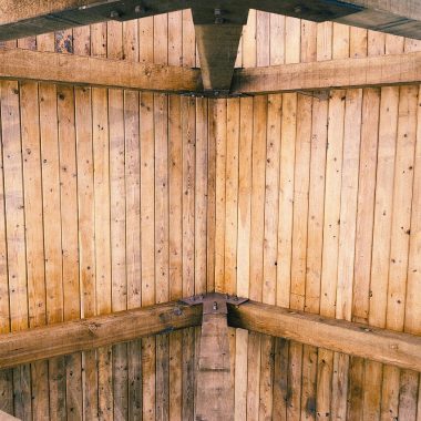 Warm woonboerderij interieur met donkere houten dakbalken, grote linnen bank en zonlicht door hoge ramen