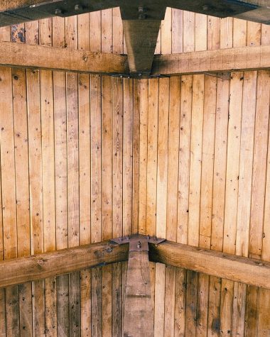 Warm woonboerderij interieur met donkere houten dakbalken, grote linnen bank en zonlicht door hoge ramen