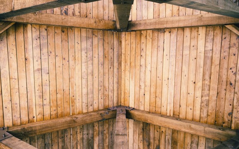 Warm woonboerderij interieur met donkere houten dakbalken, grote linnen bank en zonlicht door hoge ramen