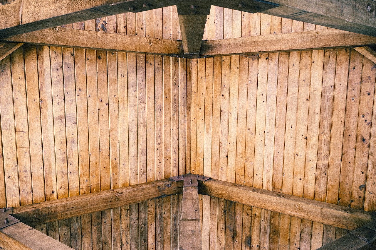 Warm woonboerderij interieur met donkere houten dakbalken, grote linnen bank en zonlicht door hoge ramen